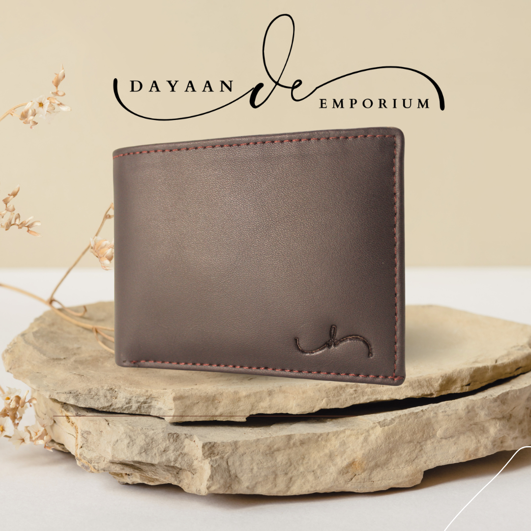 A brown leather wallet with a subtle branding logo on the bottom right corner, displayed on a natural stone surface.